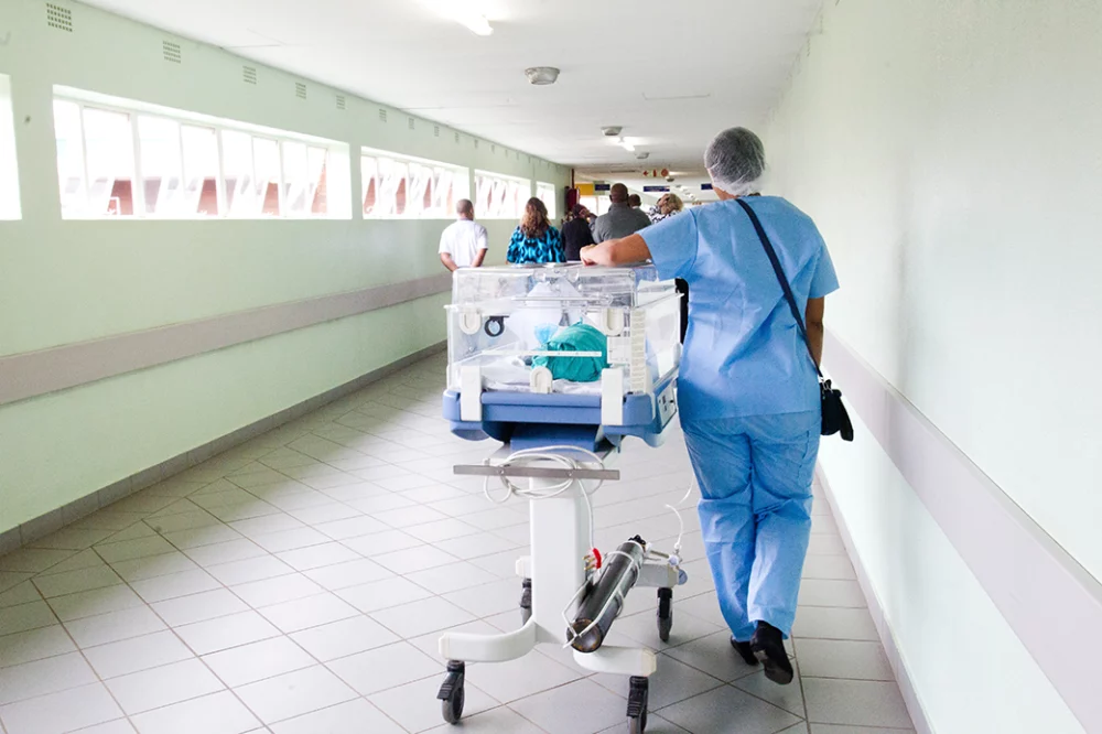 A health care worker wheels a newborn baby to the nursery.